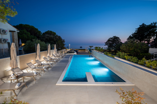 Night view of the illuminated outdoor pool at Bumblebee apartments with sun loungers and sea view